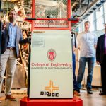A small forklift sits in a well-lit room, surrounded by people and scientific equipment. The front reads "College of Engineering: University of Wisconsin-Madison."