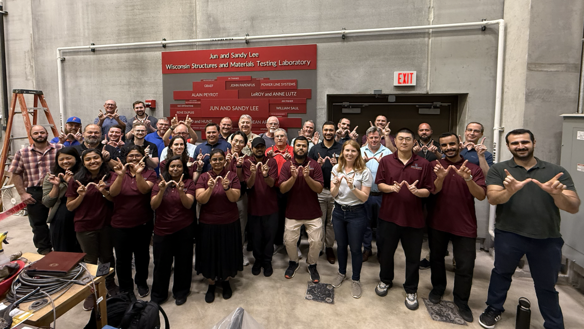 A group of people stand in a concrete testing lab and hold their hands up to form Ws.