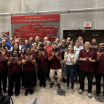 A group of people stand in a concrete testing lab and hold their hands up to form Ws.